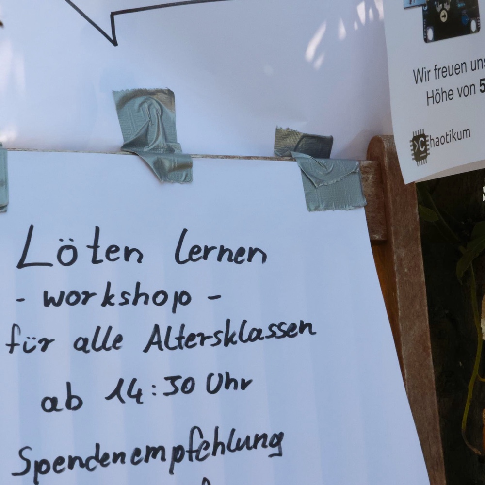 Handschriftliches Schild mit der Aufschrift: Löten Lernen Workshop für alle Altersklassen ab 14:30 Uhr. Spendenempfehlung. Oben rechts sieht man im Anschnitt ein weiteres Schild mit dem Logo des Chaotikums.